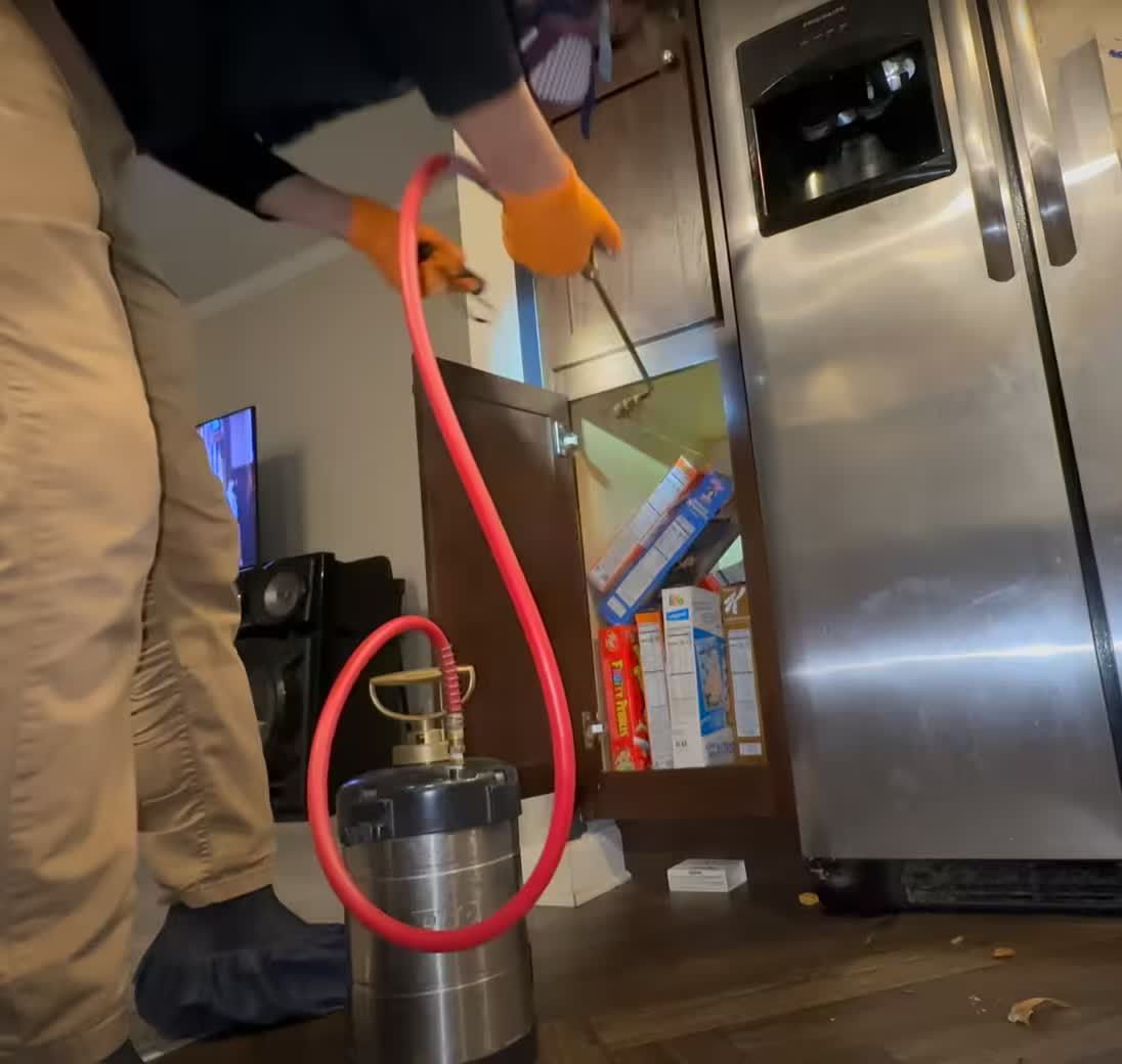 Pest control technician treating a cabinet area inside a property